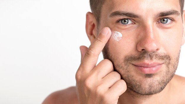 Close-up of young stubble man applying cream on her face