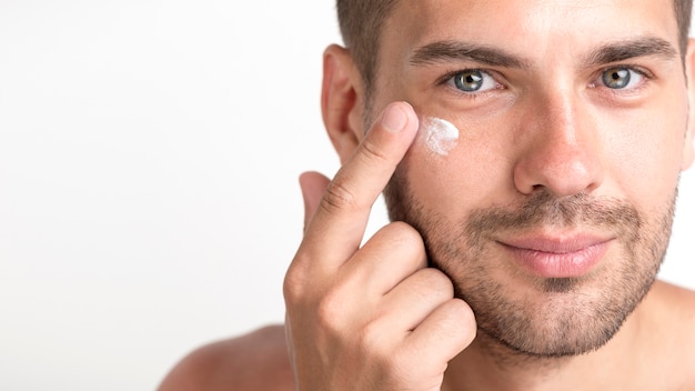 Close-up of young stubble man applying cream on her face