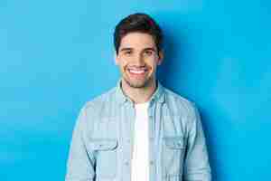 Free photo close-up of young successful man smiling at camera, standing in casual outfit against blue background