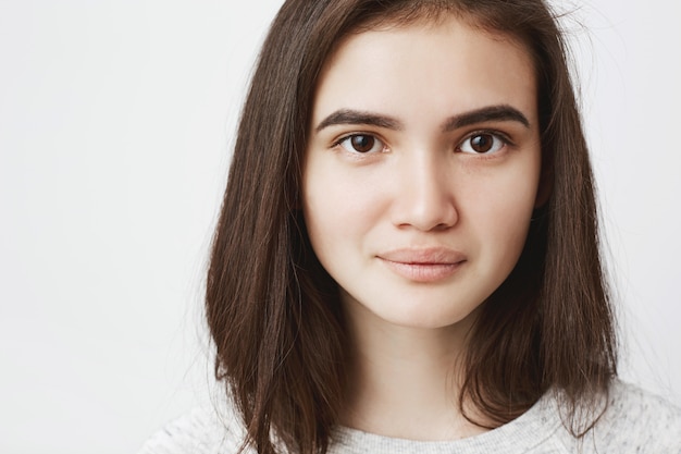 Close-up young tender female smiling with tight lips while looking