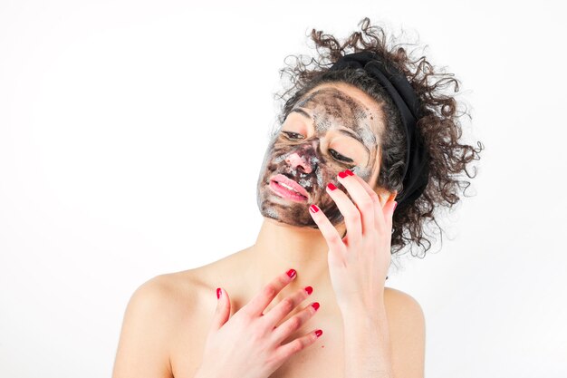 Close-up of a young woman applying black mask against white background