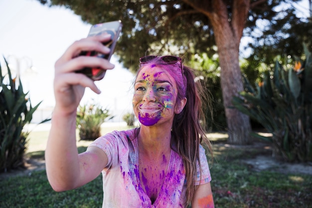 携帯電話でselfieを取ってホーリー色で覆われている若い女性のクローズアップ