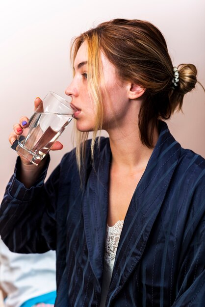 ベッドの中で水のガラスを飲むクローズアップ若い女性