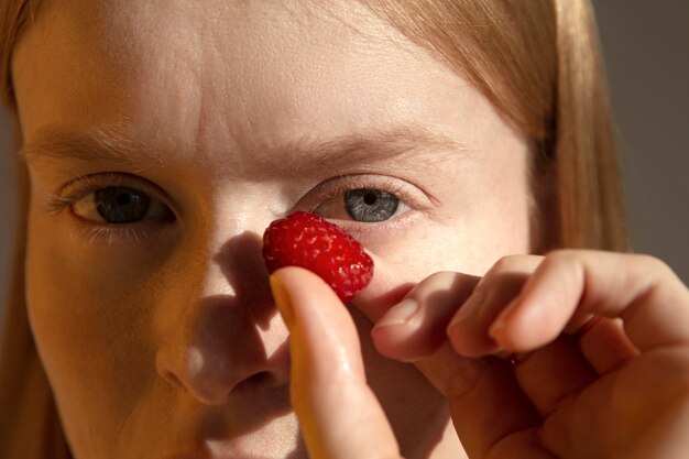 Close up young woman holding raspberry