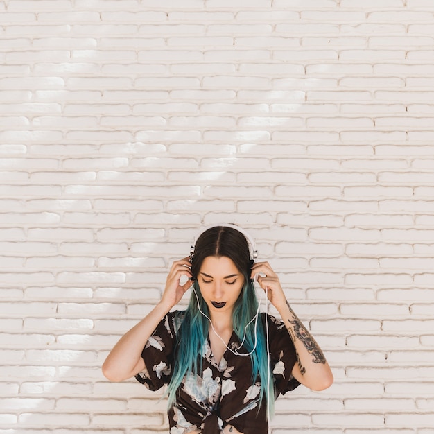 Close-up of young woman listening music on headphone against wall