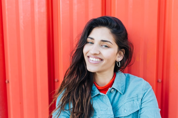 Close-up of young woman looking at camera sitting against red metallic backdrop