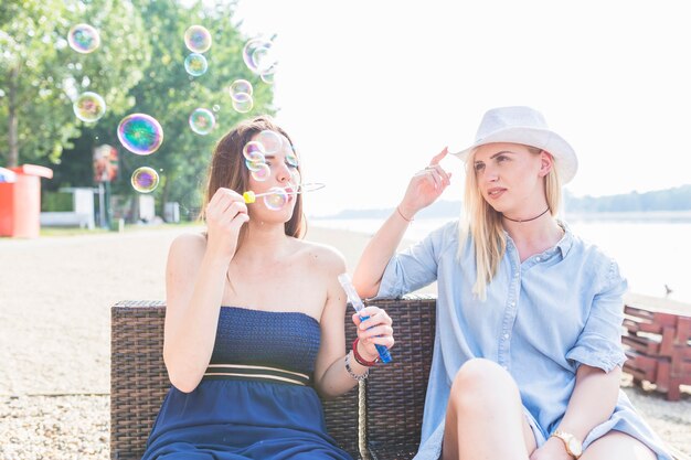 Close-up of young woman looking at friend blowing bubbles on beach