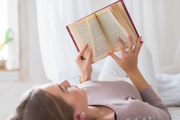 책을 읽고 침대에 누워있는 젊은 여자의 근접 촬영