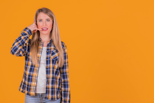 Close-up of a young woman making call gesture against an orange background