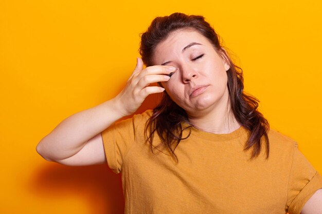 Close up of young woman rubbing hand on eyes feeling tired in studio. Sleepy person falling asleep while posing and standing over isolated background. Exhausted adult needing rest