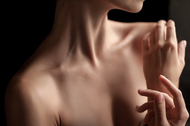 The close-up of a young woman's neck and hands  on dark background