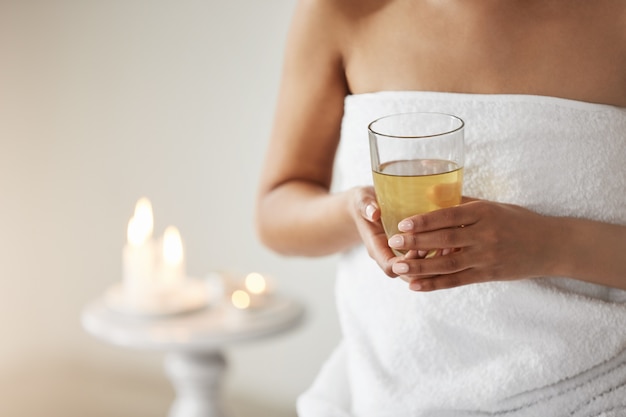 Close up of young woman in towel holding glass with green tea in spa salon.