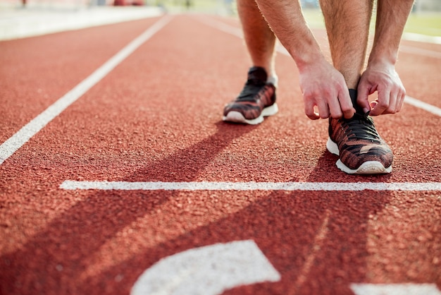 赤いレーストラックにスポーツシューズを結ぶ若い女性のクローズアップ