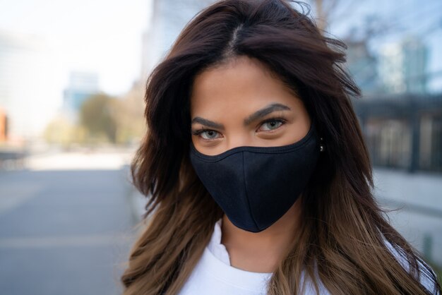 야외 거리에 서있는 동안 얼굴 마스크를 착용하는 젊은 여자의 클로즈업. 도시 개념. 새로운 정상적인 라이프 스타일 개념.