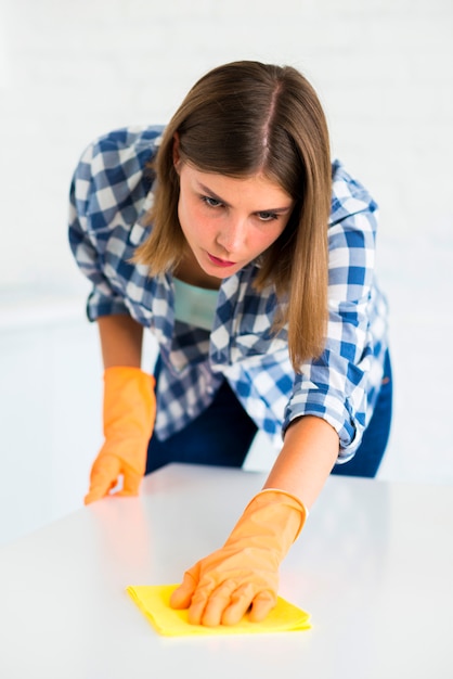 Close-up of young woman wipes white desk with yellow duster