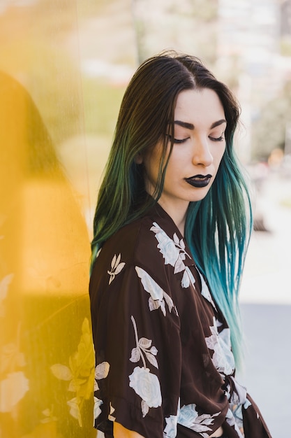 Close-up of young woman with dyed hair standing in front of yellow reflective backdrop