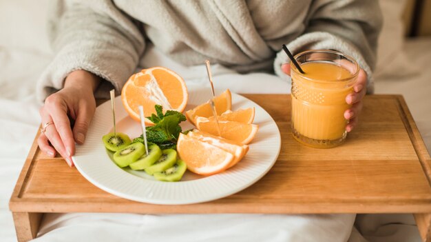 Close-up of young woman with plate of fruits and an orange juice on wooden tray