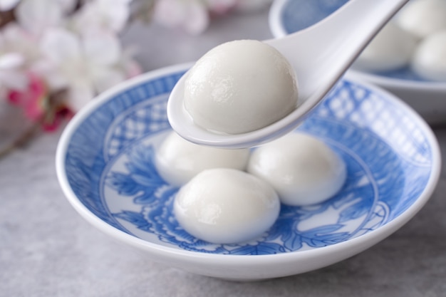 Close up of yuanxiao tangyuan (glutinous rice dumpling balls) in a bowl on gray table with flower, food for chinese lantern yuanxiao festival.