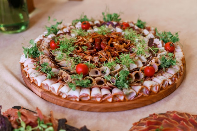Close view of appetizers on circle wooden plates full sliced different types of dried meat decorated by fresh tomato and greens served to table dinner party