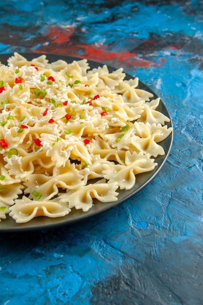 Close view of raw italian farfalle pasta with vegetables on blue background