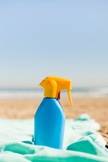 ビーチでターコイズブルーの毛布で青い日焼け止め化粧品容器を閉鎖