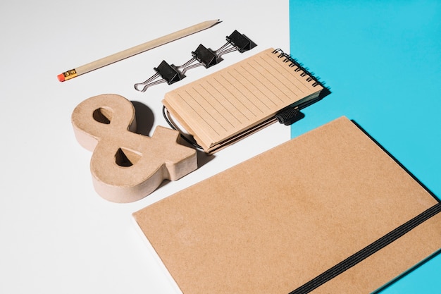 Quaderno chiuso marrone con segno e commerciale in legno; clip bulldog e blocco note a spirale