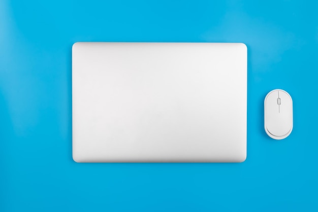 Free photo closed laptop and computer mouse on a blue background top view