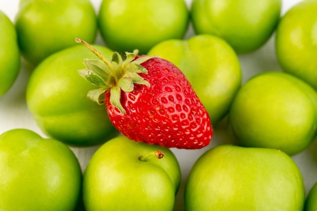 A closed up top view green cherry-plum round isolated sour fresh mellow with single strawberry on the white background fruit quality