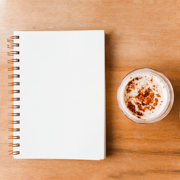 Closed white spiral notebook and coffee glass with cocoa powder