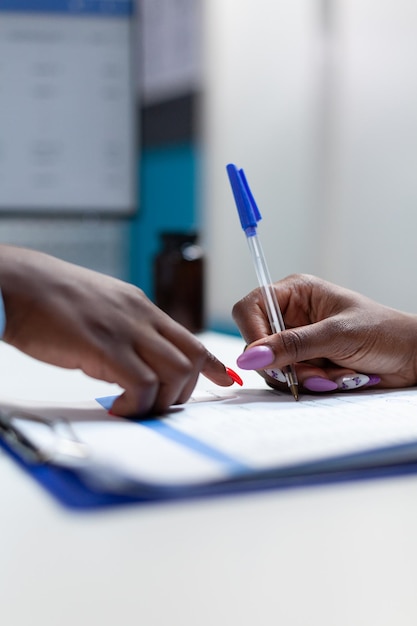 Closeup of african american physician doctor explaining healthcare treatment to sick patient while signing medical documents during clinical appointment in hospital office. Disease results papers