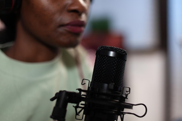 팟캐스트를 촬영하는 동안 구독자가 질문에 답하는 전문 마이크에 대고 이야기하는 아프리카계 미국인 블로거 여성의 클로즈업. 온에어 토크를 진행하는 소셜 미디어 콘텐츠 제작자