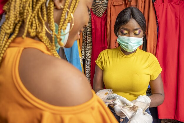 Closeup of an African female with latex gloves and a facemask paying with cash at a shop