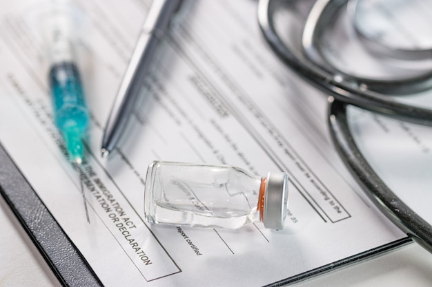 Closeup of an ampoule and a needle syringe on a document with a phonendoscope