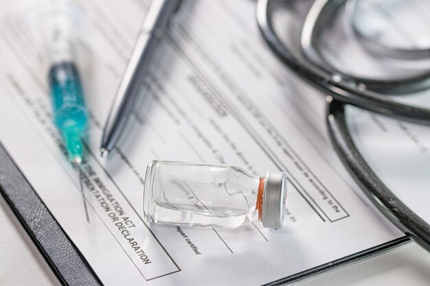 Closeup of an ampoule and a needle syringe on a document with a phonendoscope