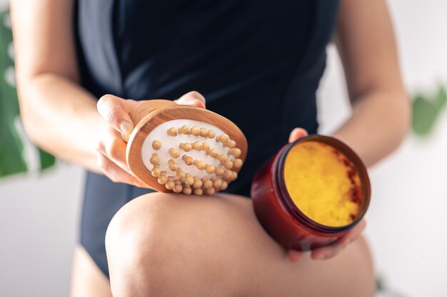 Closeup of anticellulite massage brush and body scrub in female hands