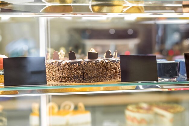 Closeup of appetizing fresh chocolate cake behind glass of showcase in pastry shop or cafe