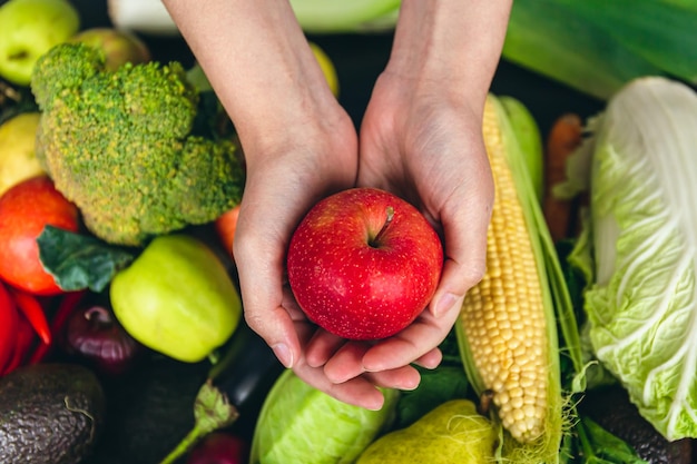Крупным планом яблоко в женской руке на размытом фоне с овощами