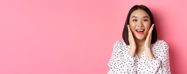 無料Photo きれいな肌の顔に触れ、カメラを見つめる美しいアジアの女性のクローズアップは、立って驚いた