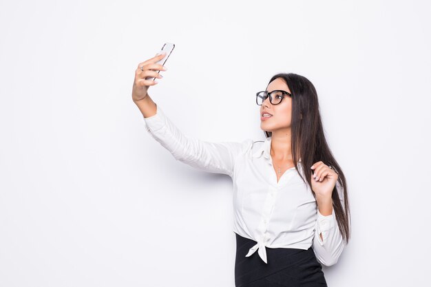 Primo piano di bella donna allegra di affari in occhiali che fanno la foto del selfie su bianco