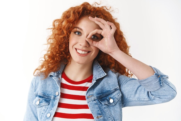 Free photo closeup beautiful positive young ginger curlyhaired girl brighten up day pure sincere smily white teeth show okay ok sign eye look through optimistic standing pleased white background