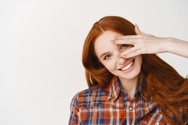 Closeup of beautiful redhead lady with blue eyes and pale skin smiling at camera standing over white background Copy space