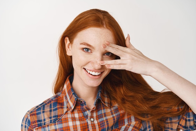 Closeup of beautiful redhead lady with blue eyes and pale skin smiling at camera standing over white background