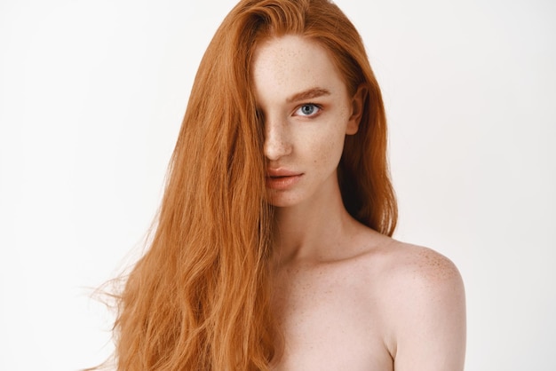관능적 인 흰색 배경을 응시하는 카메라 창백한 여성 빨간 머리 모델을보고 길고 건강한 빨간 머리를 가진 아름 다운 젊은 여자의 근접 촬영
