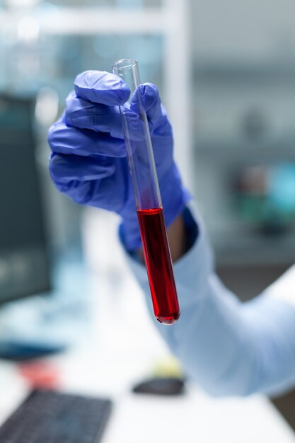 Closeup of biologist chemist holding medical test tube with blood developing virus treatment during biochemistry experiment. Scientist doctor working at healthcare treatment in clinical laboratory