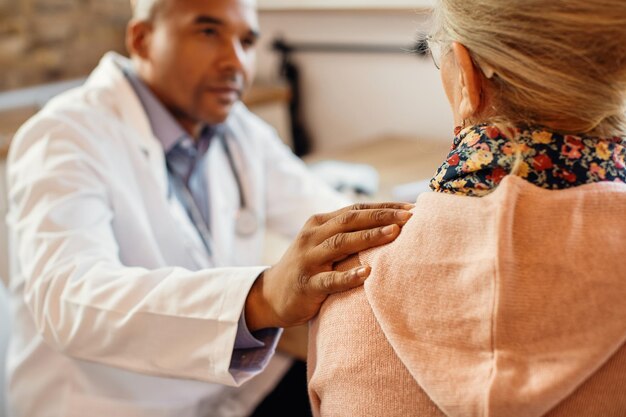 Closeup of black doctor comforting senior woman during home visit