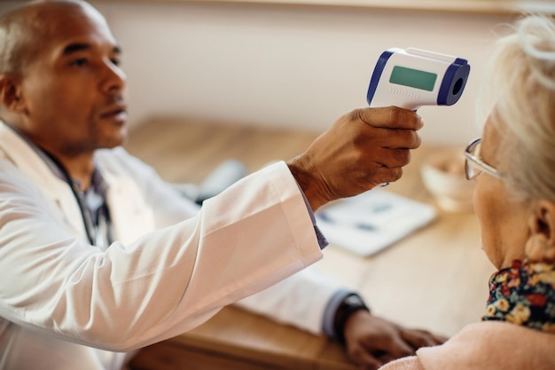 Closeup of black doctor measuring body temperature of senior woman with infrared thermometer