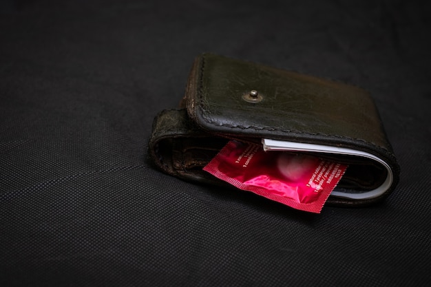 검정색 배경에 빨간색 콘돔이 있는 근접 촬영 검은색 가죽 지갑