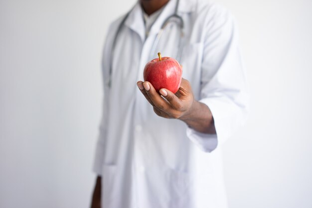 Closeup of black male doctor holding and offering red apple. 
