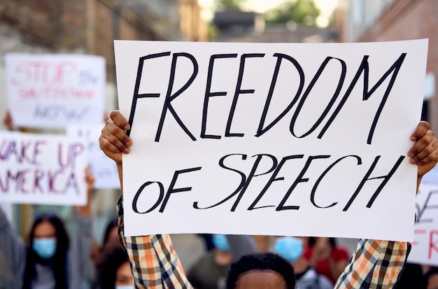 Closeup of black man protesting with large group of people and holding a placard with freedom of speech inscription