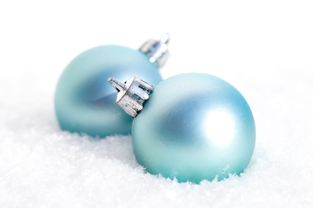 Closeup of blue Christmas bulbs in the snow in front of a blurry background